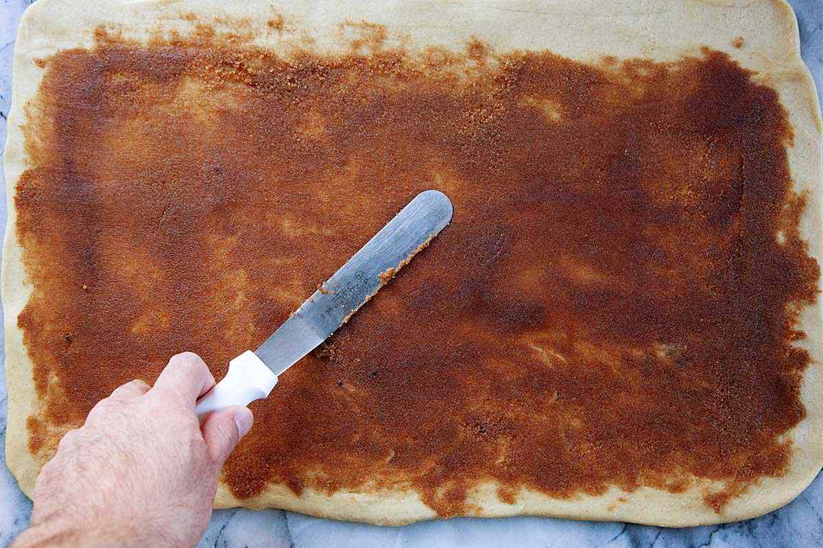 Overhead view of an offset spatula spreading king cake filling over the entire rectangle of dough.