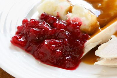 A closeup of cranberry sauce on a plate with mashed potatoes, gravy, and turkey
