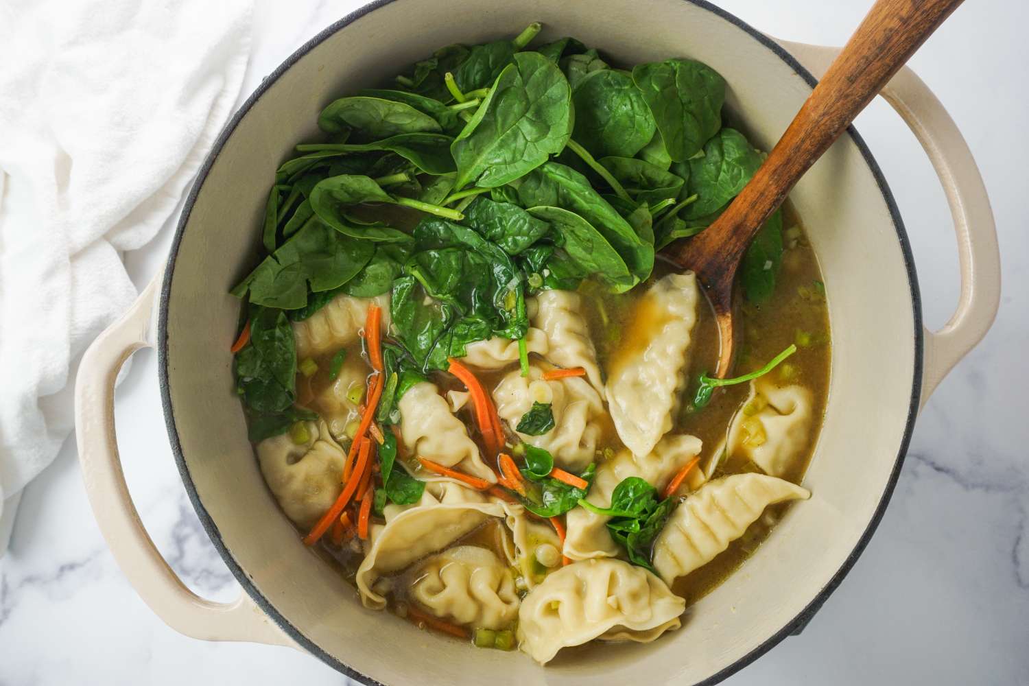 A pot of soup with dumplings spinach and carrots served with a wooden spoon