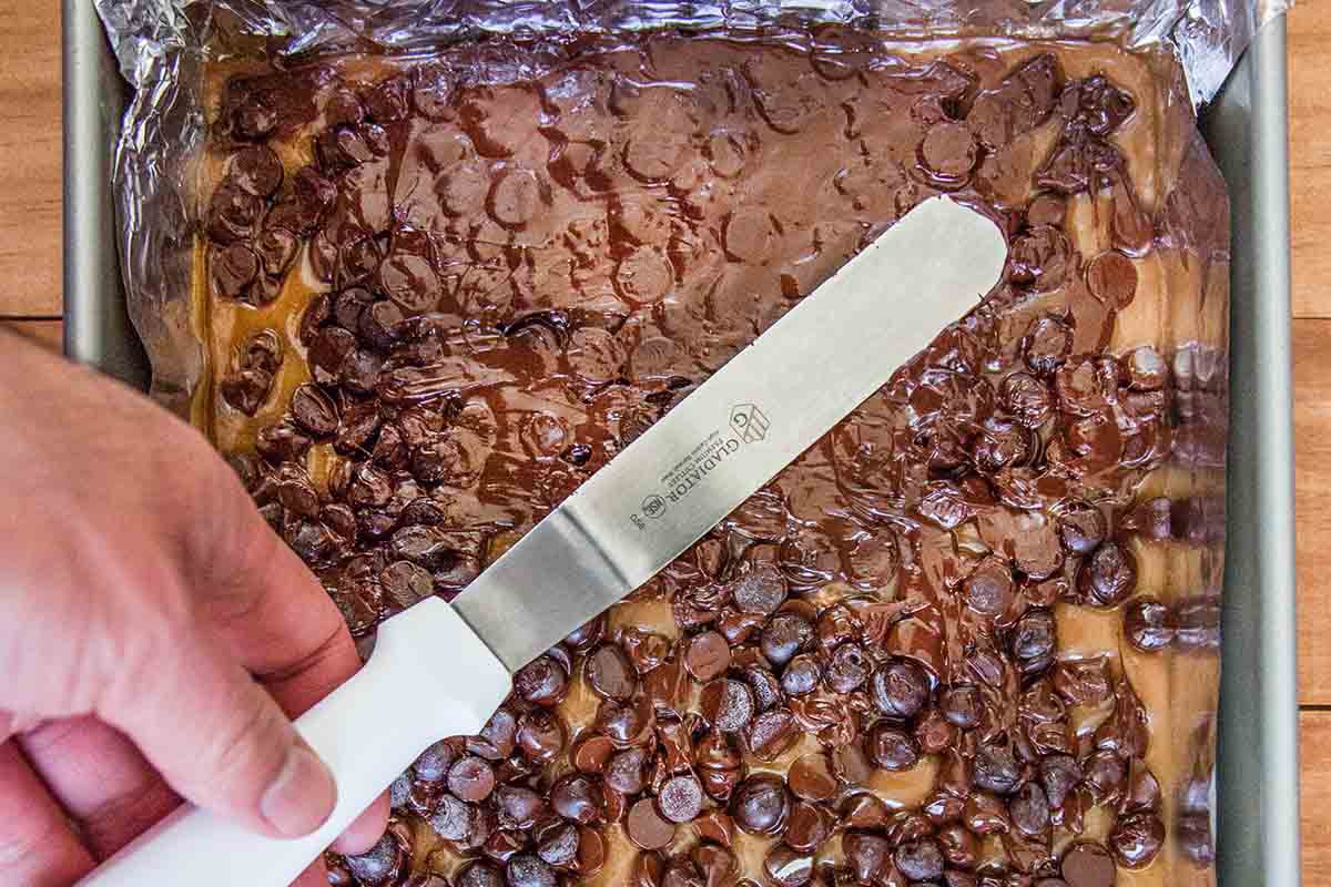 Off-set spatula spreading chocolate topping to make easy toffee.
