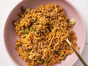 Overhead view of a pink bowl of pork and garlic noodles with a fork and topped with green onions