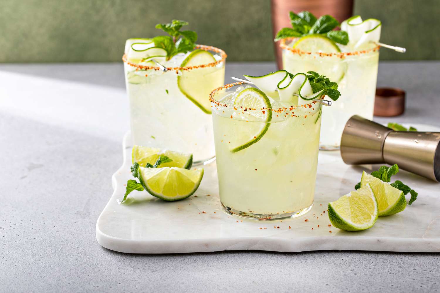 Three margarita glasses with lime garnish and mint leaves on a white tray with lime wedges nearby