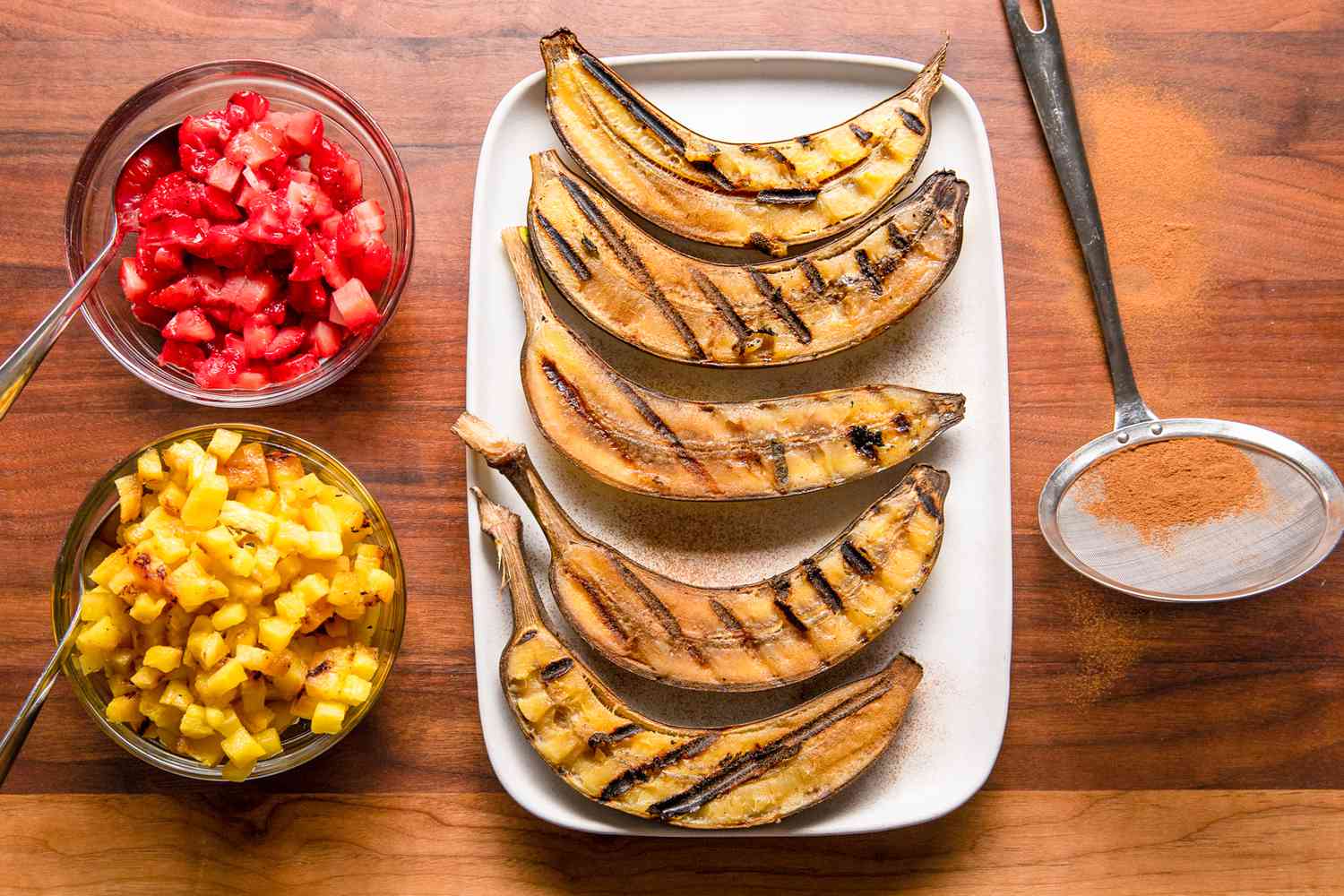 Sliced Bananas on a Platter and Sprinkled With Ground Cinnamon, and on the Counter Next to the Platter, Two Bowls (One With Diced Strawberries and Another With Diced Pineapples)