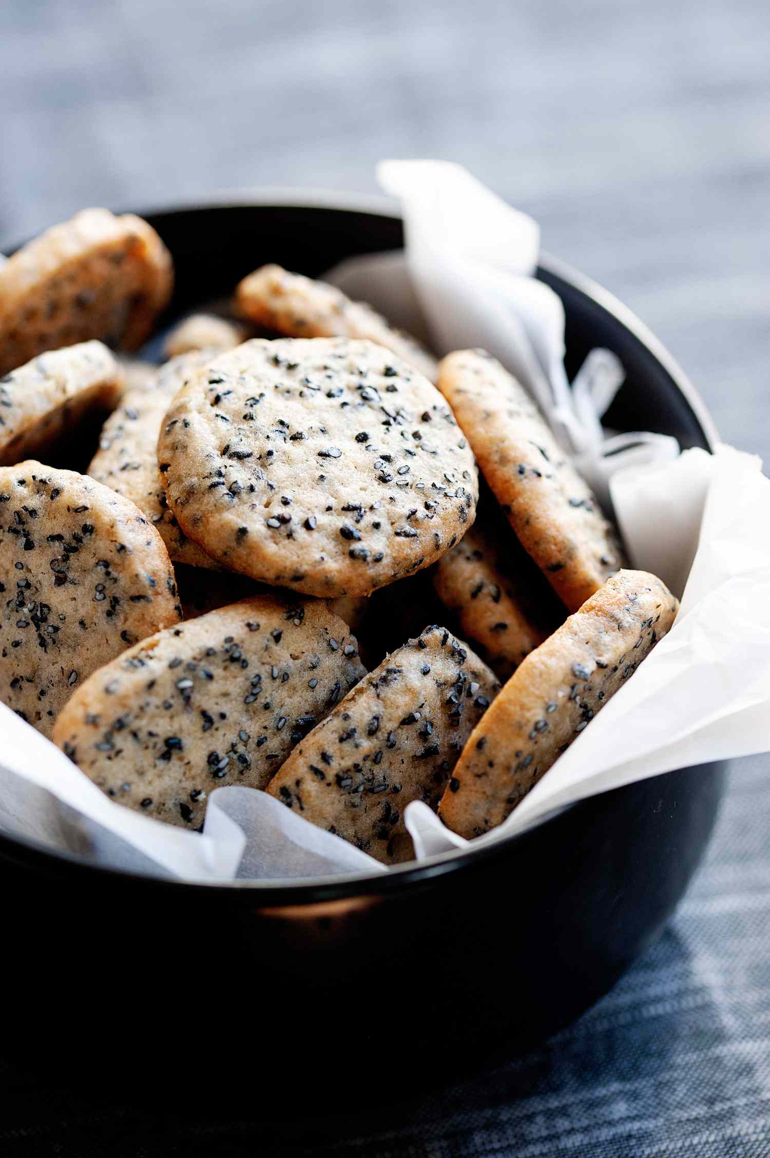Buttery sesame cookies in a cookie tin lined with white tissue paper. 