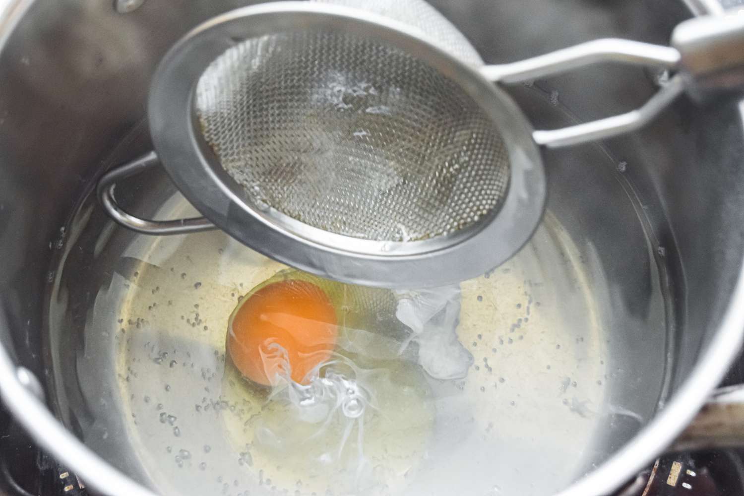 A cracked egg dropped into a pot of simmering water 