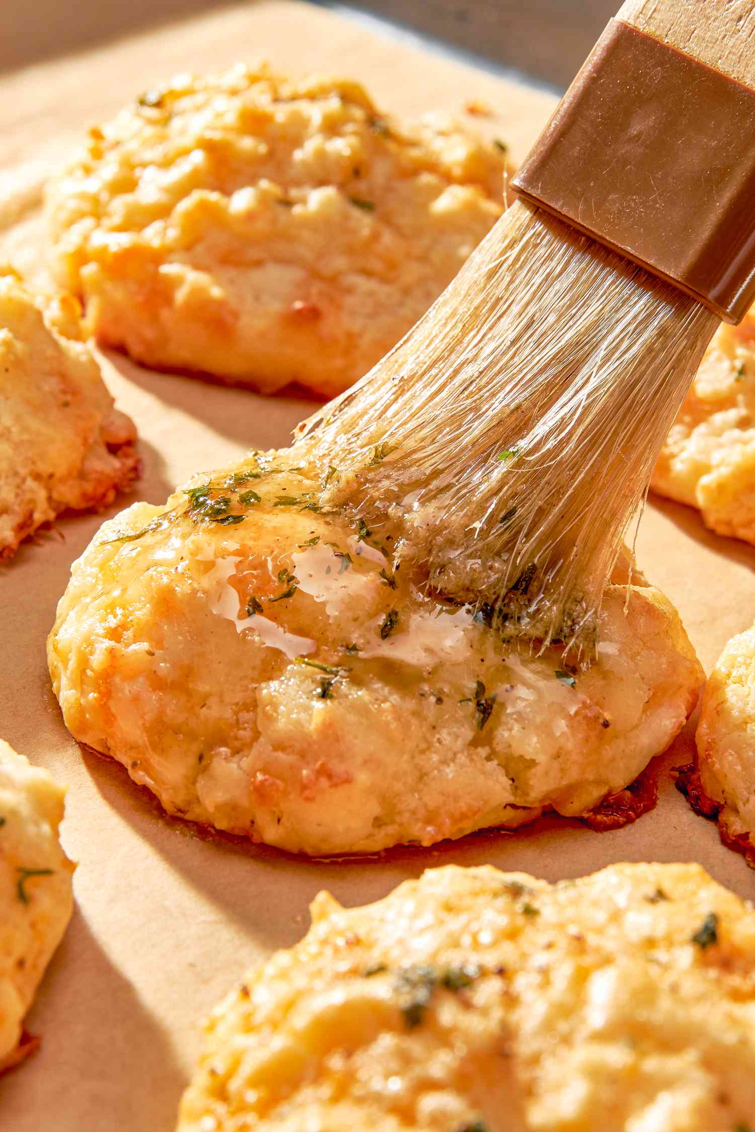 Garlic Old Bay butter brushed onto baked copycat Red Lobster cheddar bay biscuits on a baking sheet