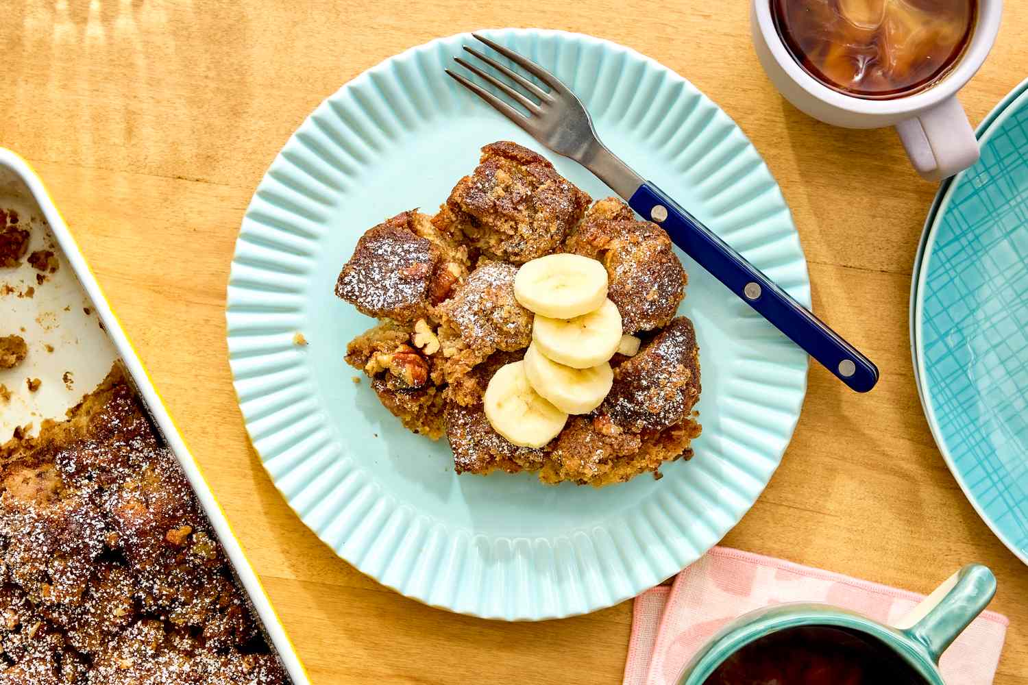 Banana bread breakfast casserole served on a plate with sliced bananas and a fork with coffee and additional casserole nearby