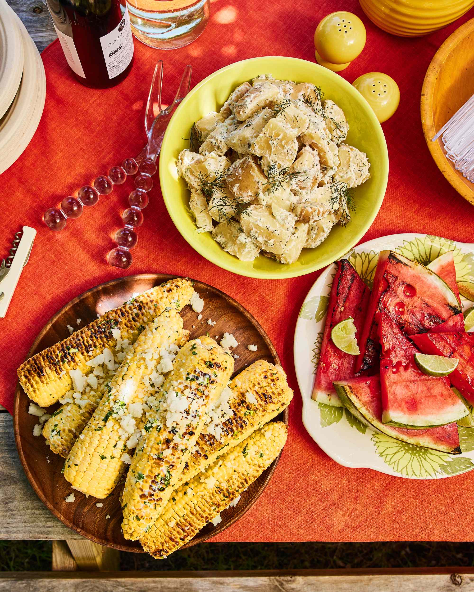 Corn on the cob, potato salad, and slices of watermelon on a picnic table