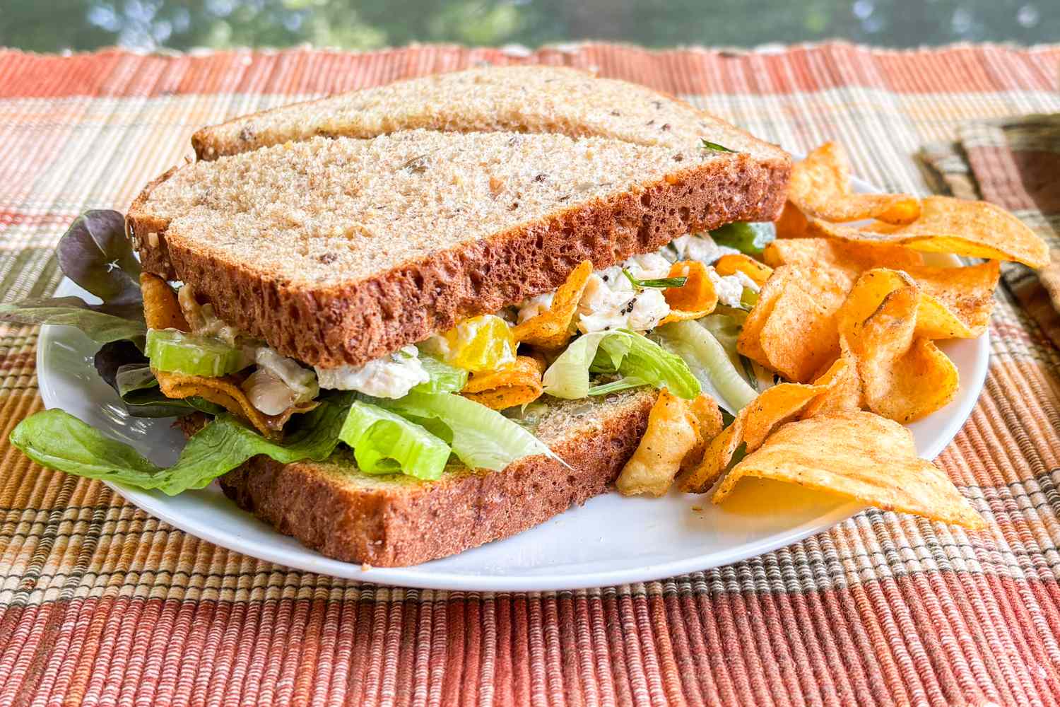 A chicken salad sandwich on wholegrain bread with lettuce and chips on a plate
