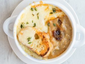 A bowl of French onion potato soup topped with melted cheese herbs and a slice of bread