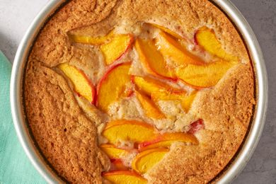 Baked peach spoon cake in a round pan featuring peach slices in a golden uneven cake top