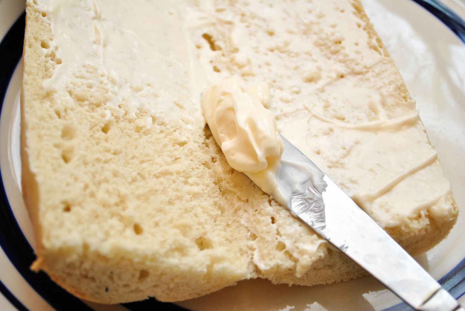 Mayonnaise being spread on a piece of white bread with a butter knife
