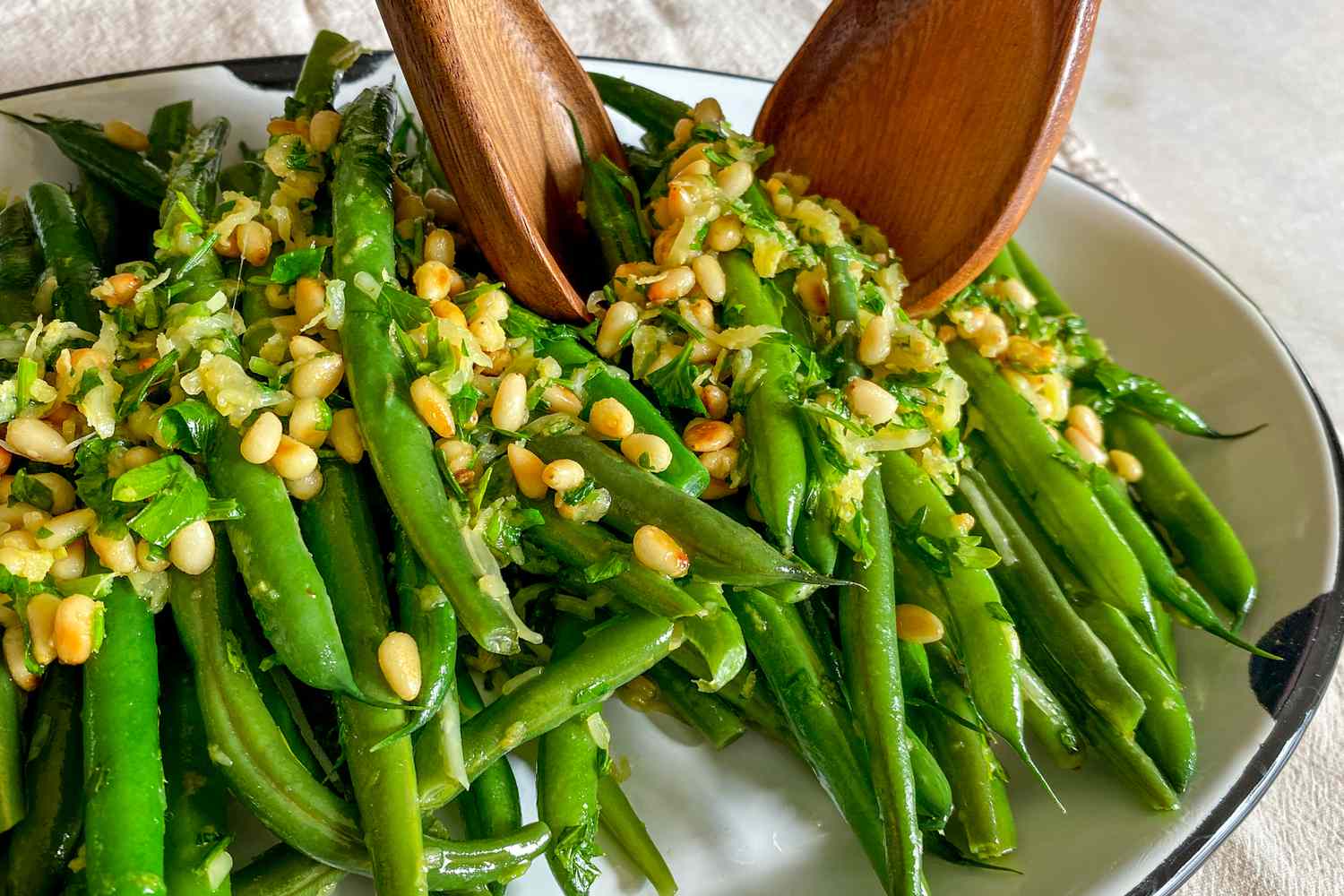A close-up of pine nut-topped green beans being served from a platter