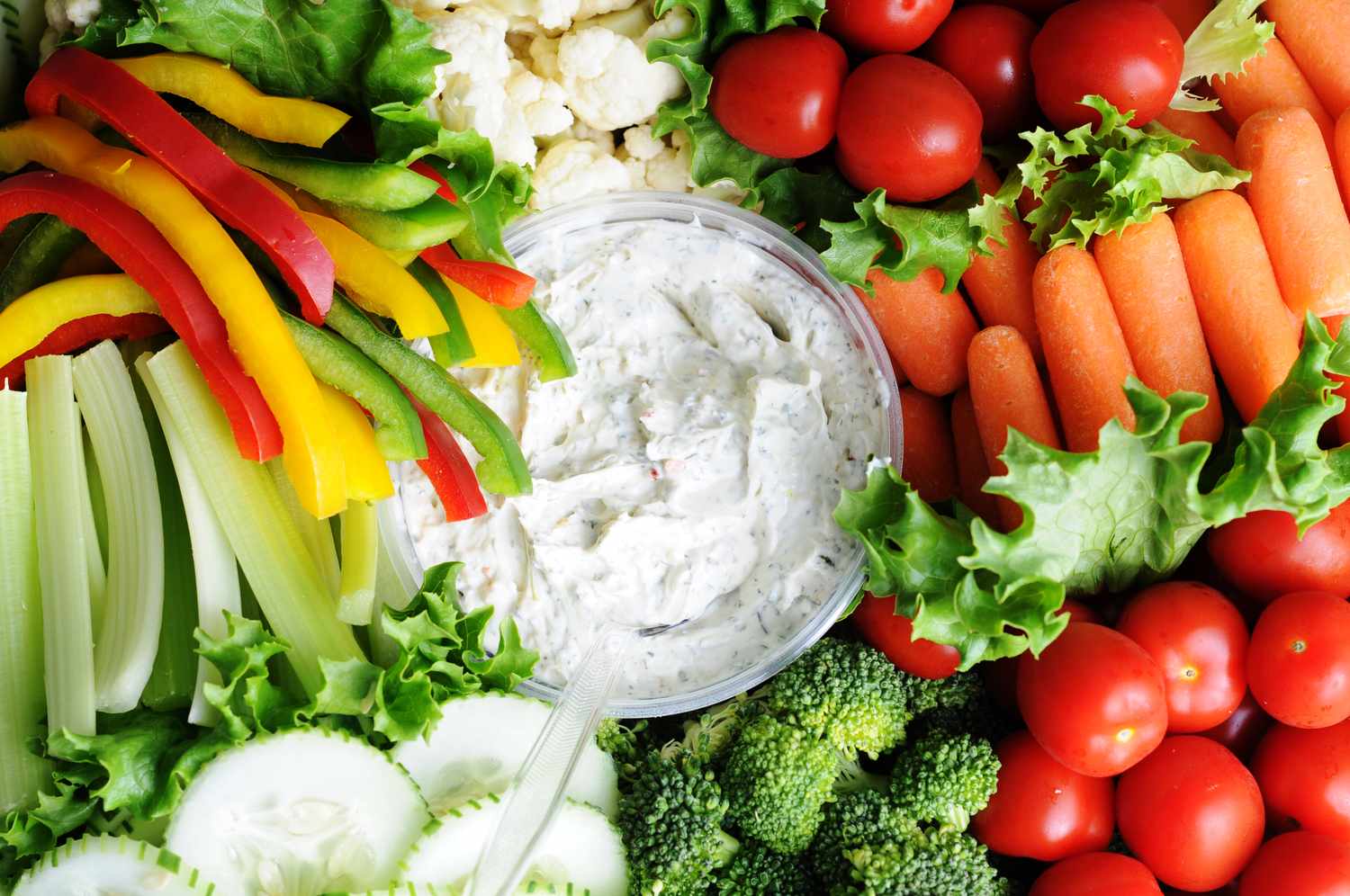 A vegetable tray with assorted fresh cut vegetables and a bowl of dip in the center