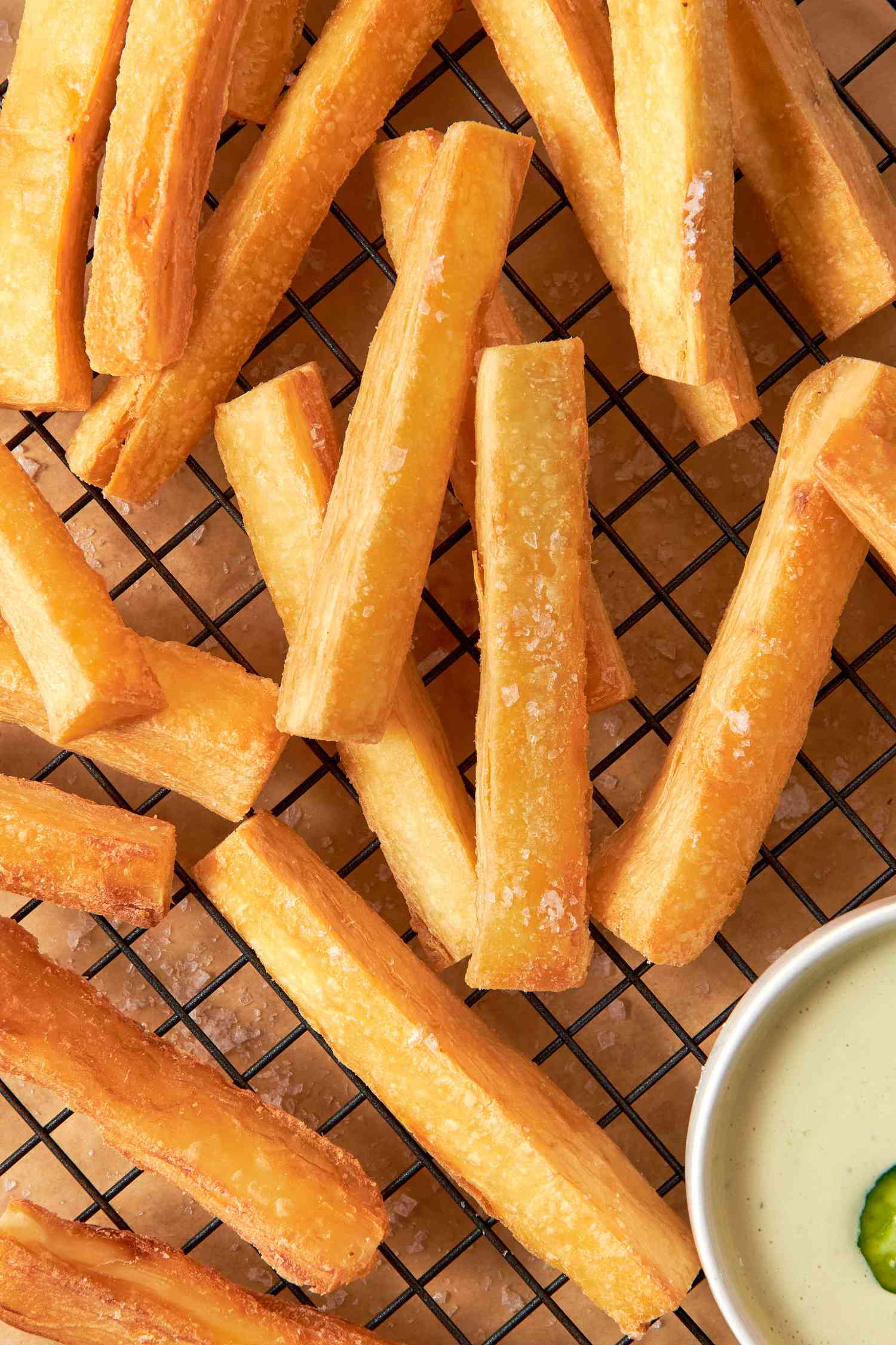 Yuca Fries on a Cooling Rack With a Bowl of Spicy Mayo, and Underneath the Cooling Rack, Parchment Paper