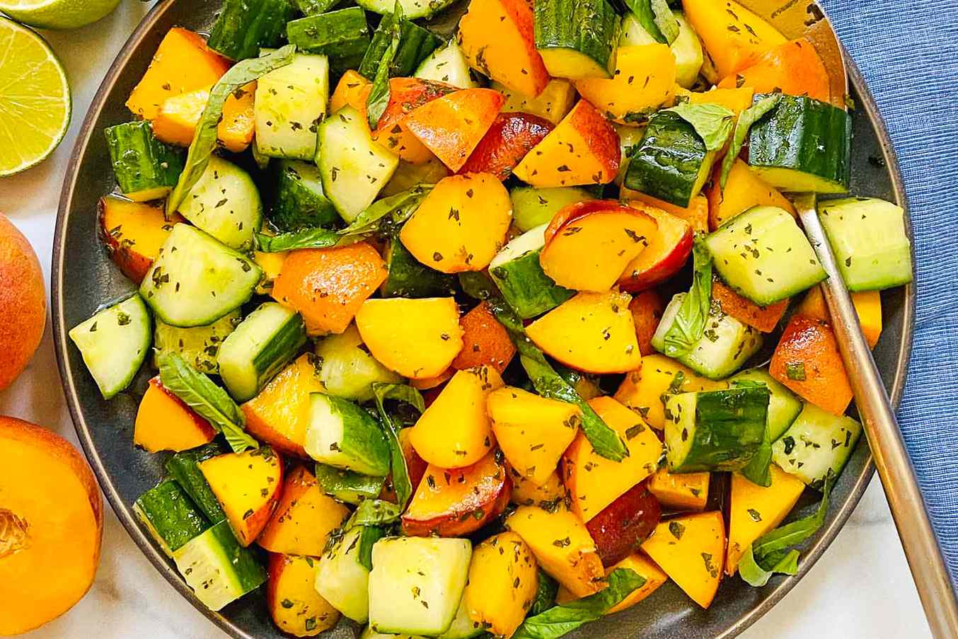 A bowl of peach, cucumber, and basil salad garnished with fresh basil leaves