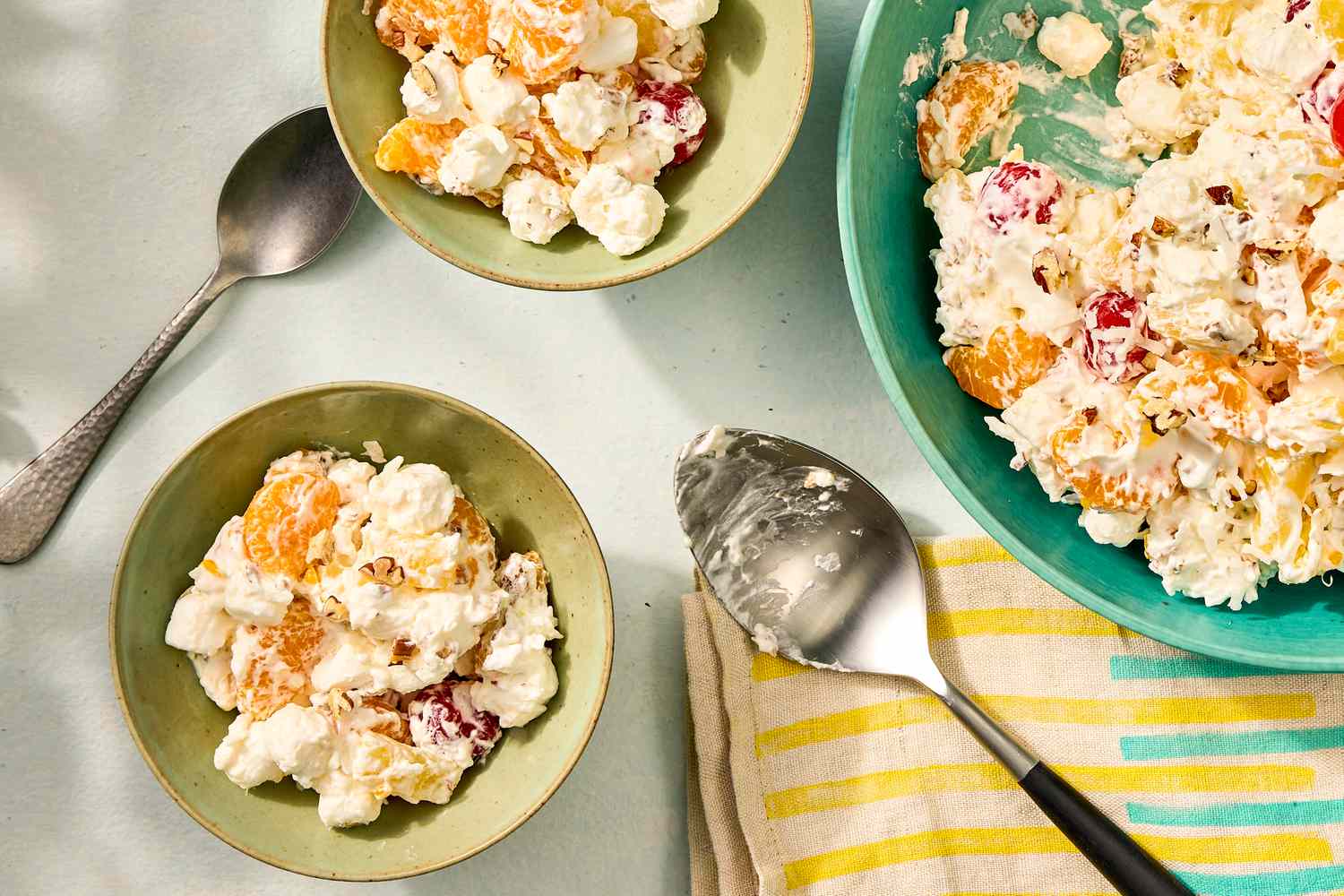 Serving bowls and a large bowl of ambrosia salad with a serving spoon nearby