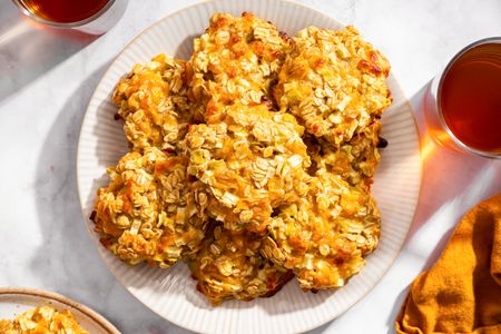 A plate of apple cheddar oat cookies surrounded by glasses of a beverage on a table