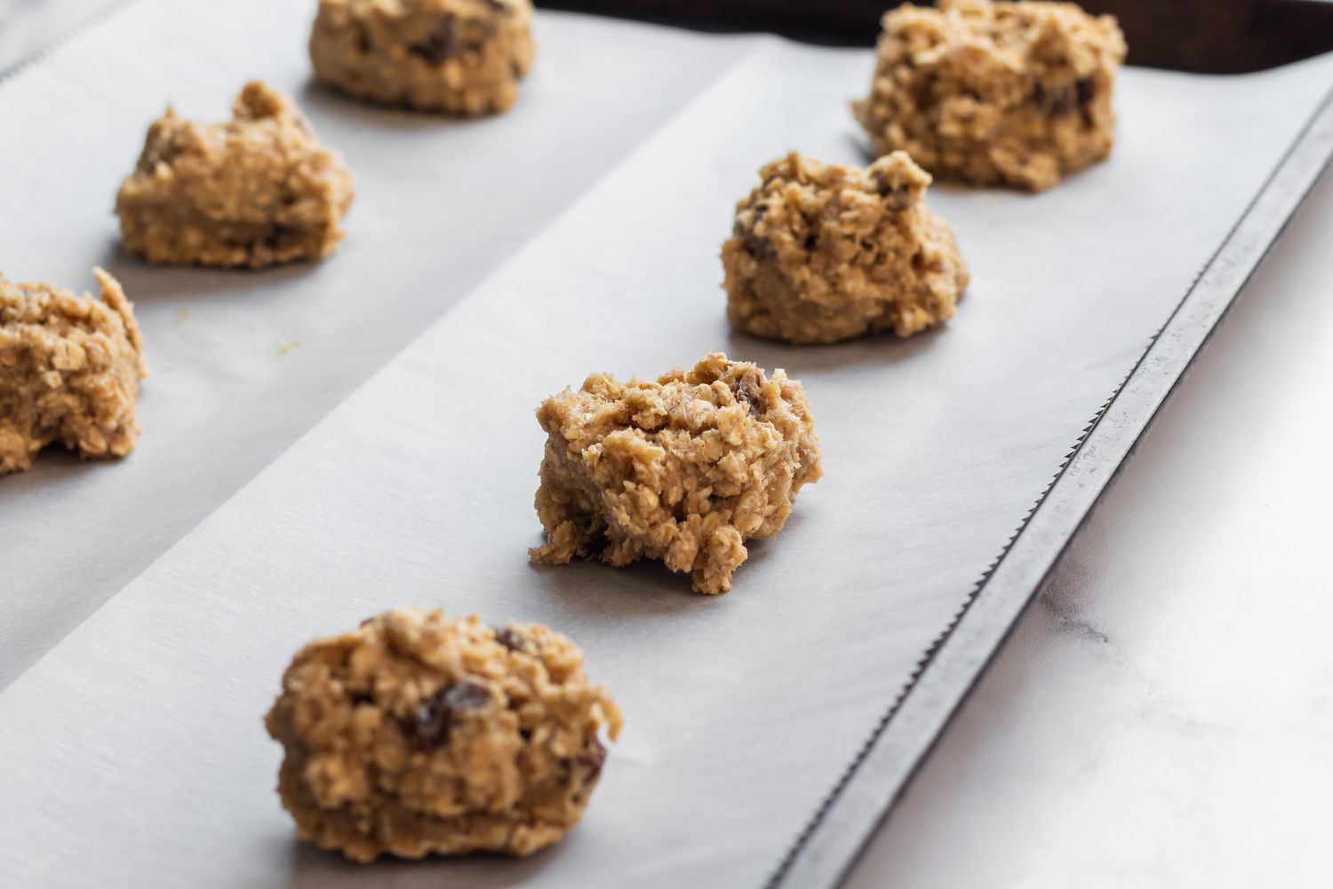 Oatmeal Raisin Cookies scooped on a parchment lined baking sheet.