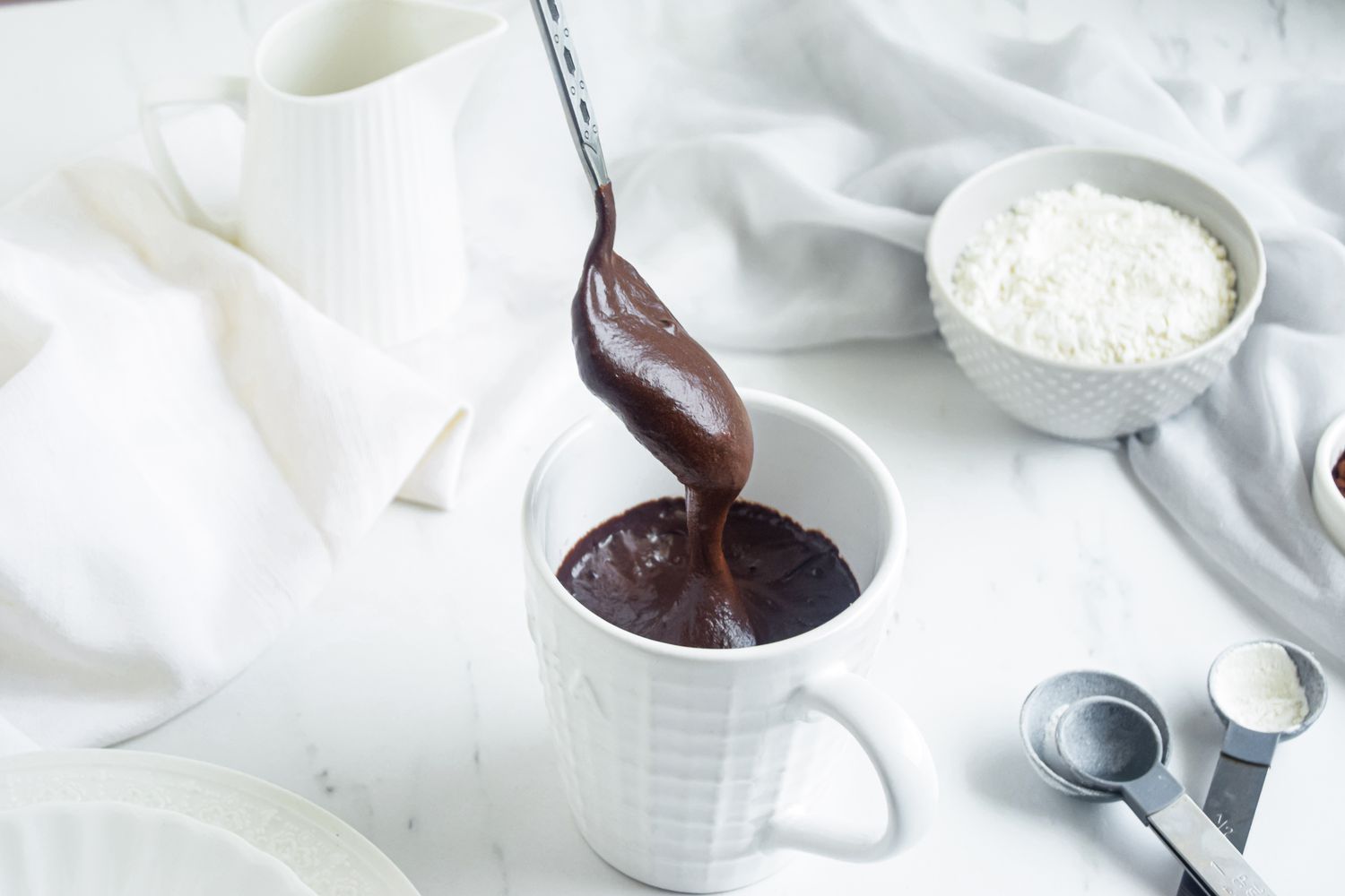 Spooning chocolate into a white cup to make a Brownie in a Mug recipe.
