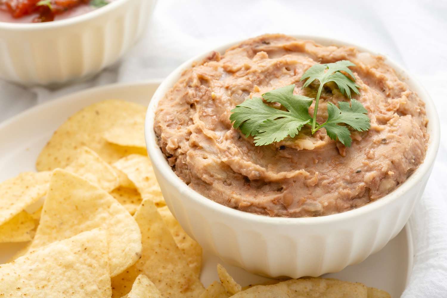 A bowl of refried beans served with chips and topped with cilantro 