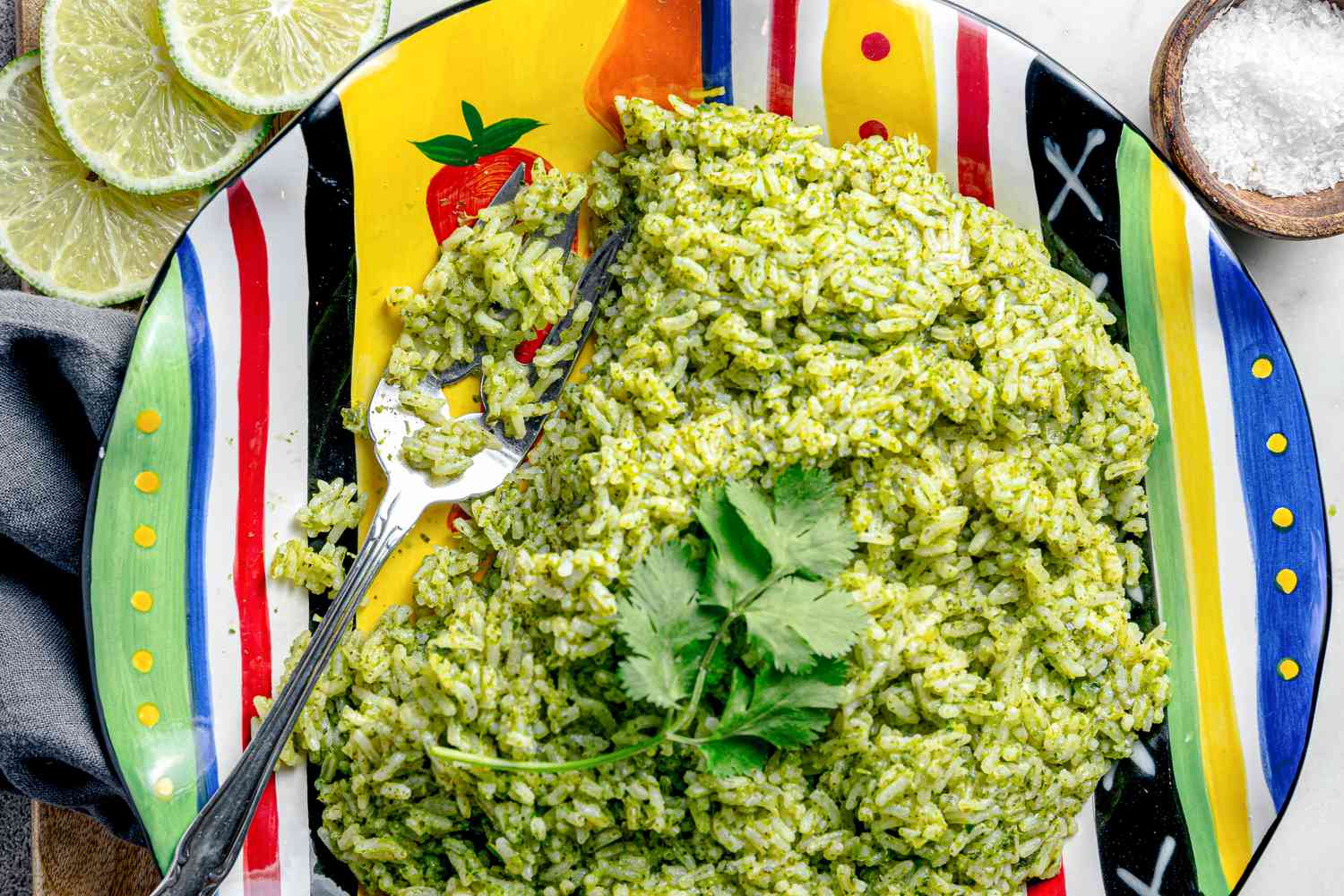 Microwave Arroz Verde on a Plate with a Fork and Surrounded by Lime Wheels, a Bowl of Course Salt, and a Table Napkin