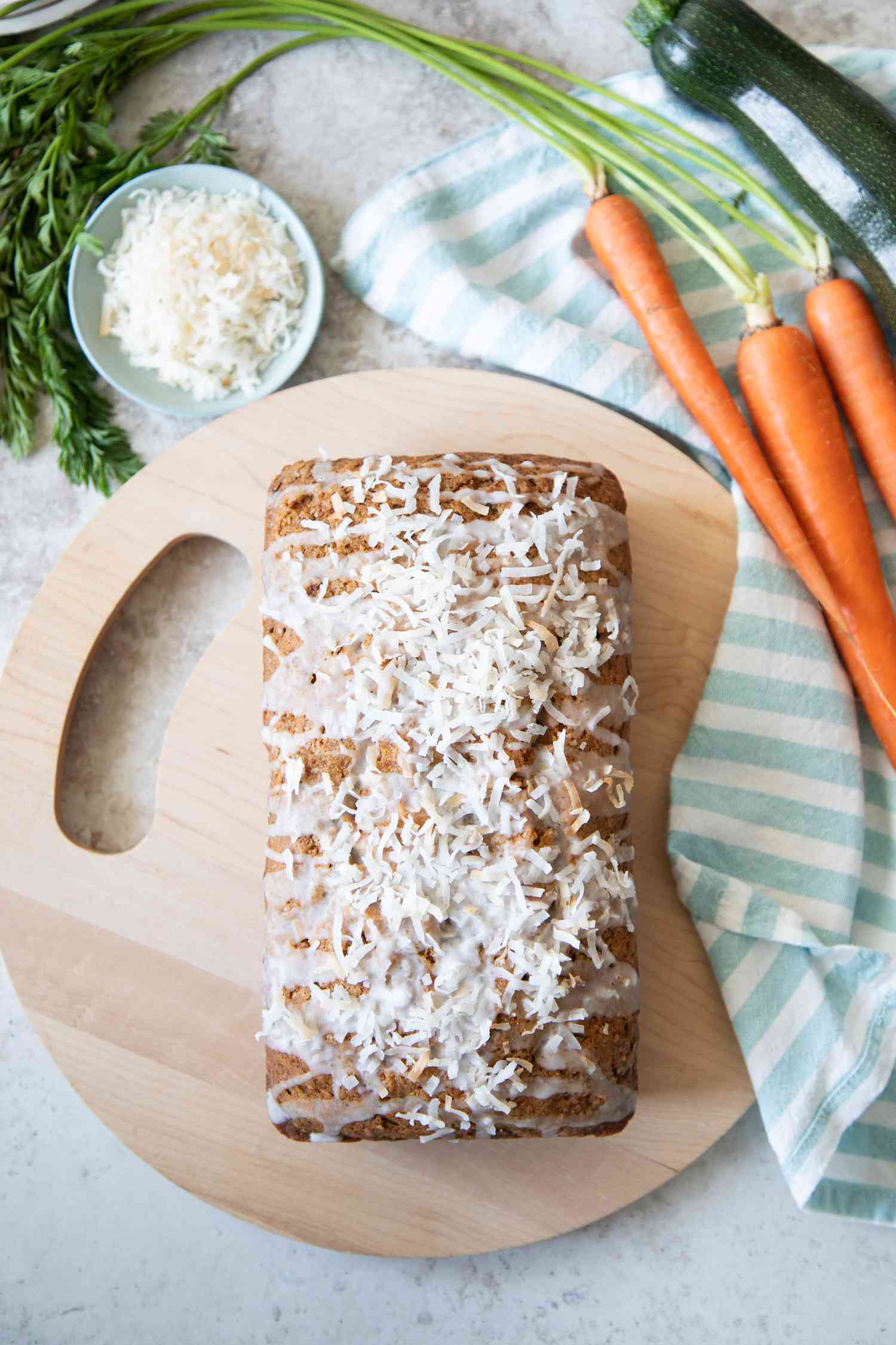 Zucchini Carrot Bread on Circular Wood Board, Surrounded by Carrots, Zucchini, and Coconut Flakes 