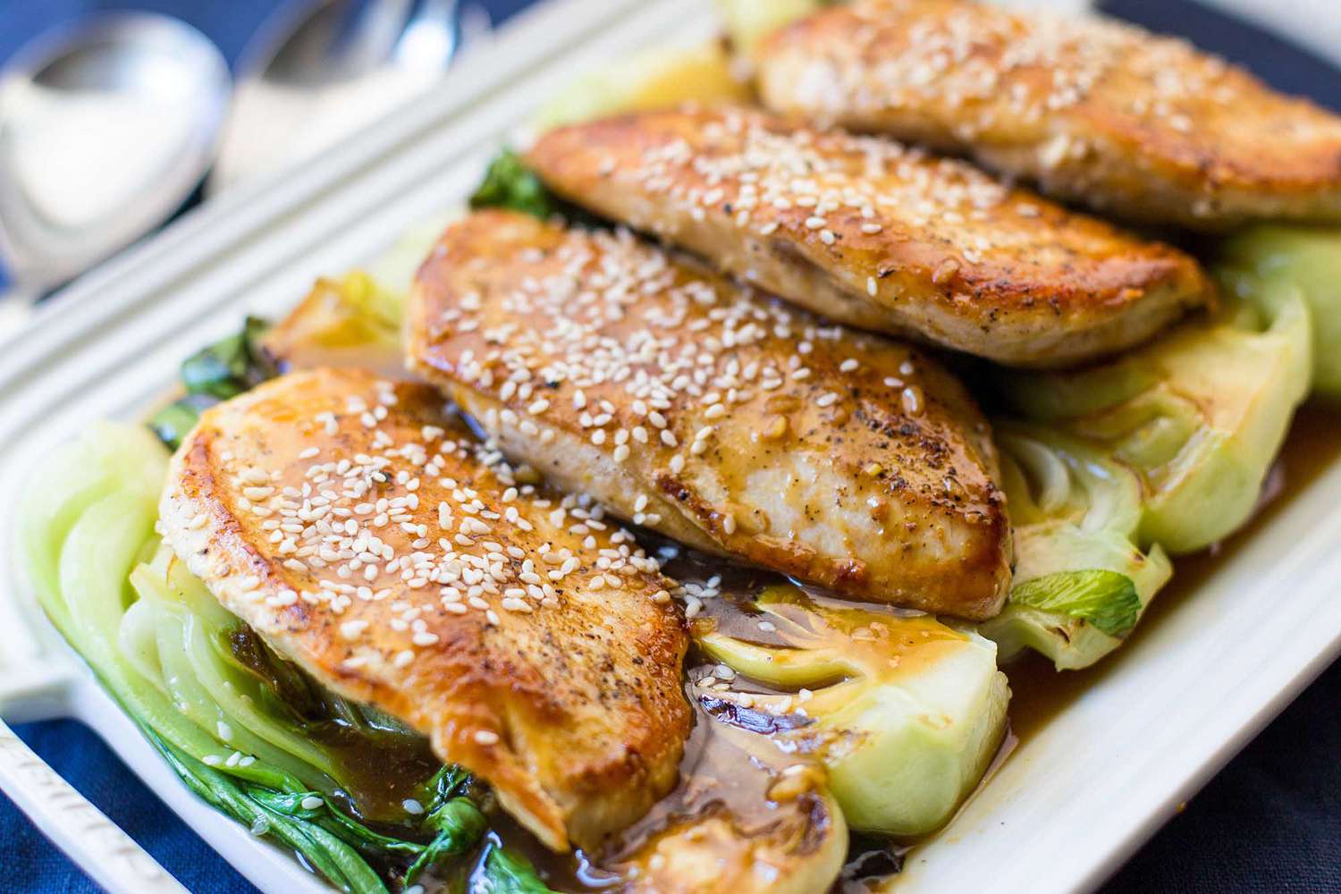 Cooked chicken breasts on bok choy garnished with sesame seeds on a serving platter