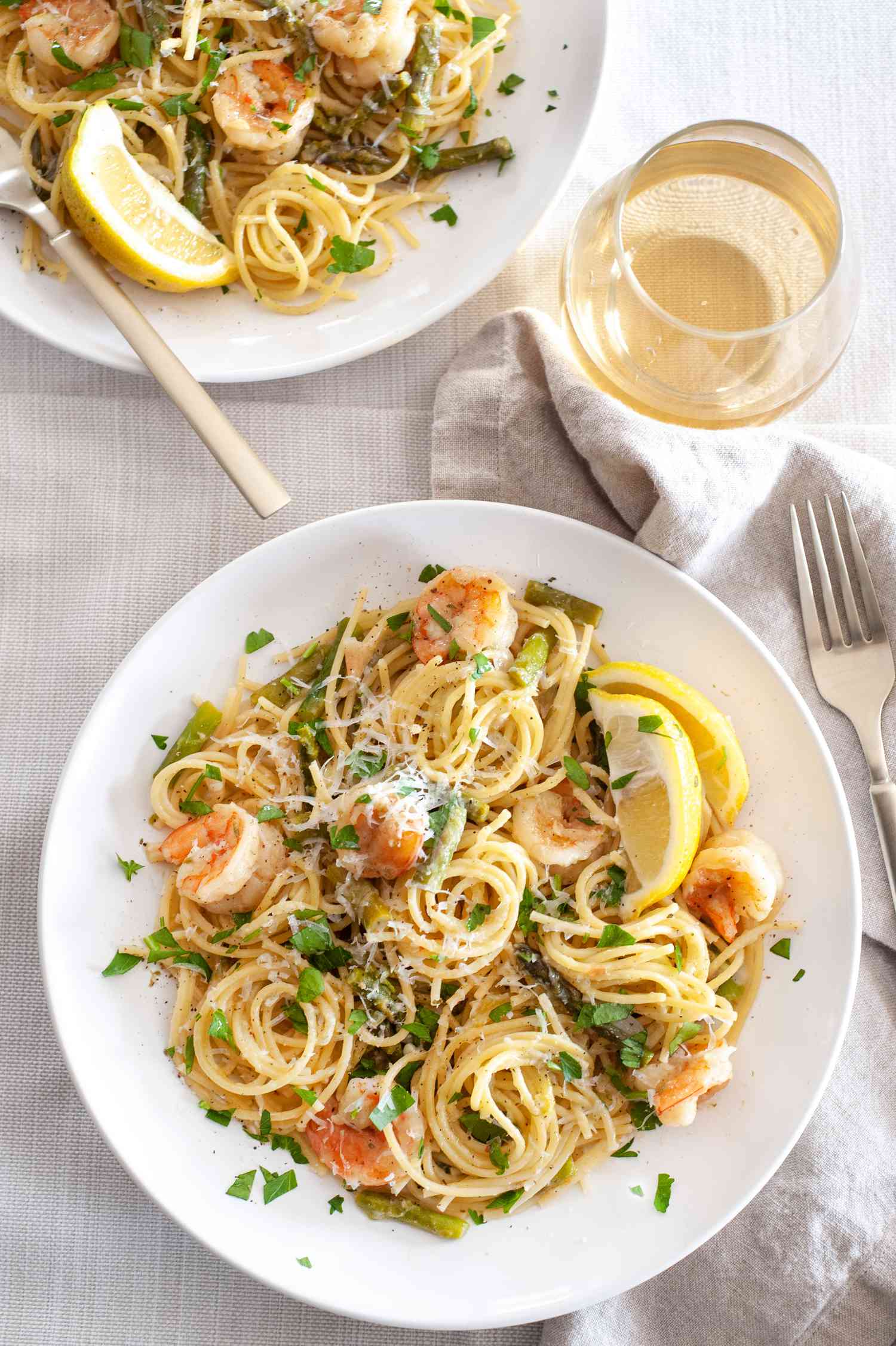 Shrimp and Asparagus Pasta on a Plate Surrounded by Glass, Fork, and Bowl of Pasta