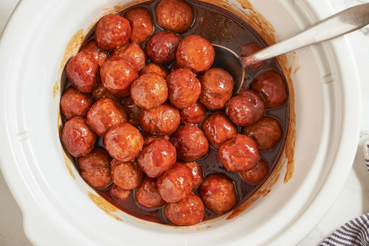 A slow cooker filled with meatballs in a sauce with a spoon for serving