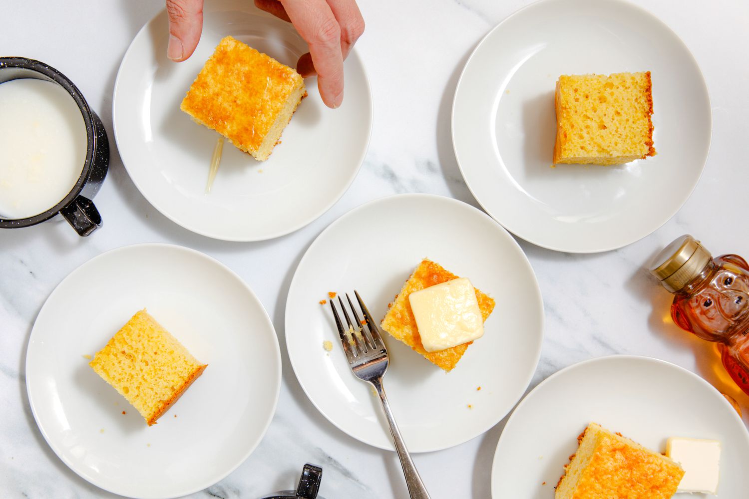 slices of cornbread on small plates, one topped with butter and someone reaching for another 