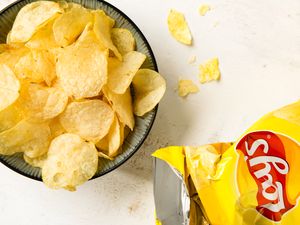 A bowl of potato chips next to an open bag of Lays chips chips scattered nearby