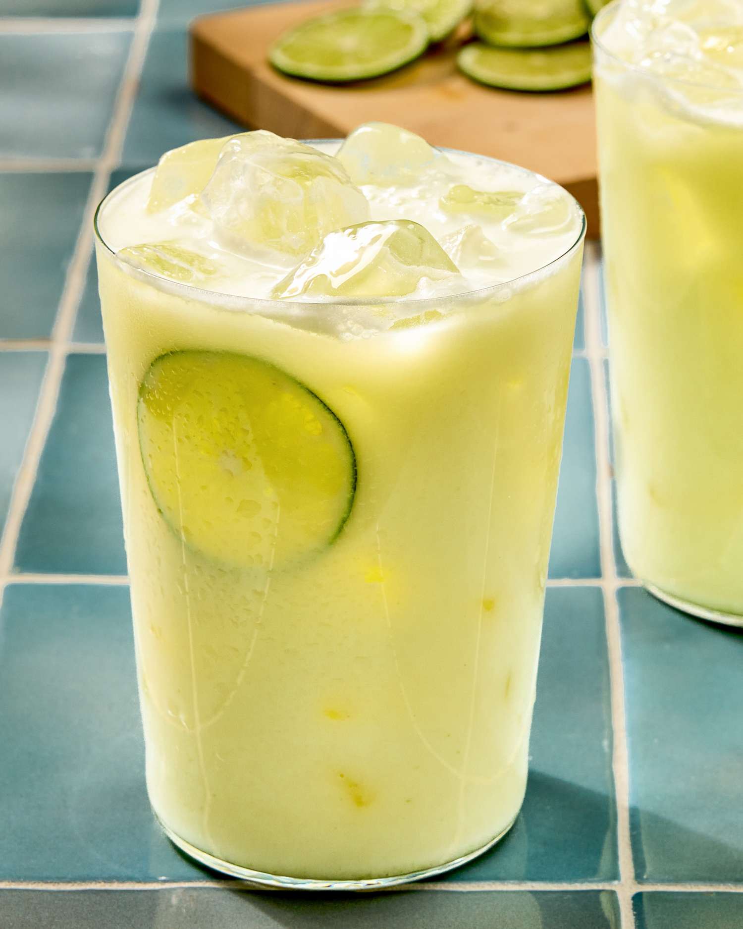 Glass of creamy limeade with ice cubes and lime slice, other similar drink in background