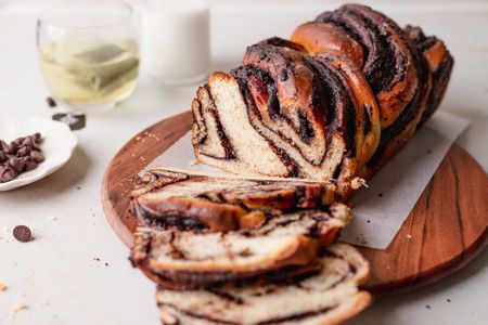 Semi-sweet chocolate babka on a wooden serving platter and three slices cut and laid in front.