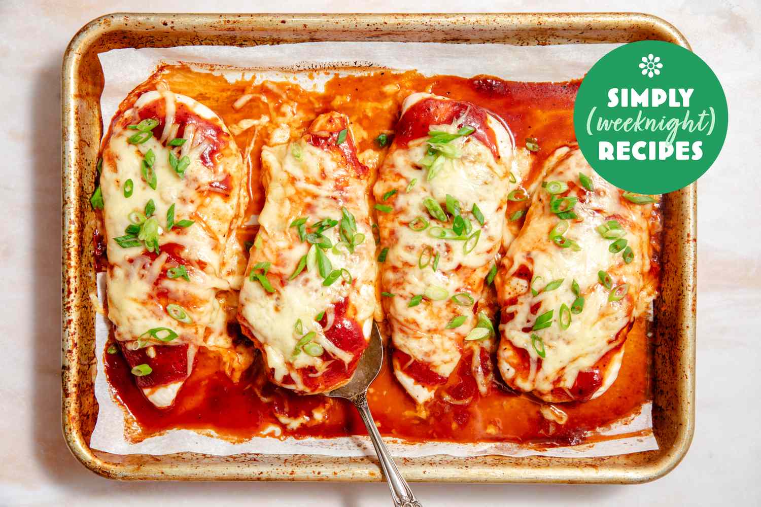 Baked chicken breasts topped with melted cheese and green onions on a baking sheet with a spoon Simply Weeknight Recipes logo in corner