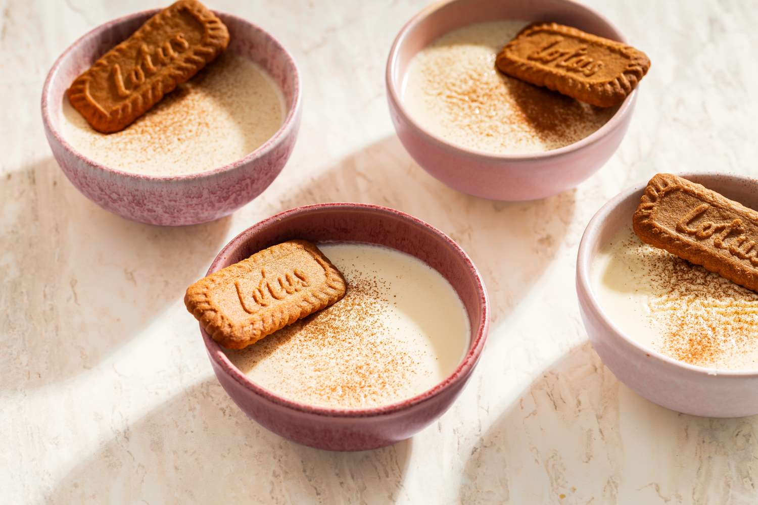 Bowls of panna cotta topped with Lotus biscuits on a light surface