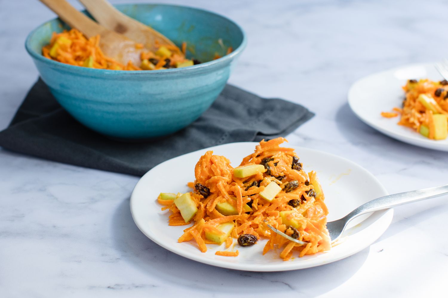 A plate of Classic Carrot Salad with the remaining salad in a bowl behind it.