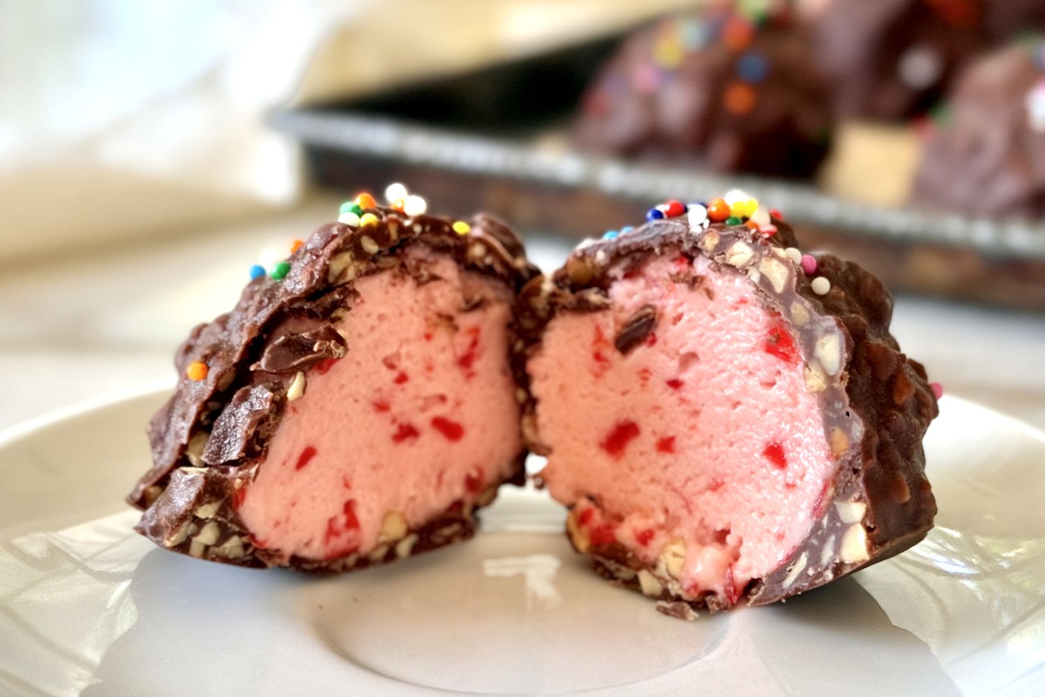 Cherryflavored dessert covered in chocolate interior revealed showing pink filling with red bits topped with sprinkles on a plate