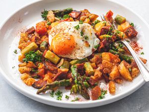 A white plate with Spanish Style Migas with Asparagus, Chorizo, Bacon, and Eggs.