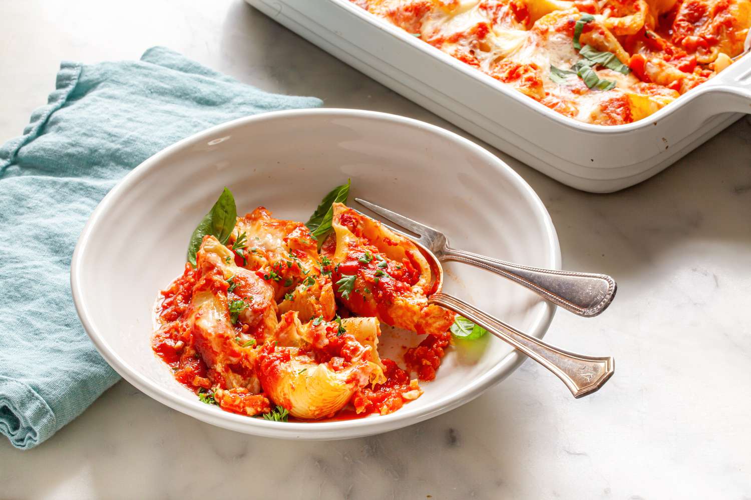 Stuffed Shells in a Bowl with Utensils and, in the Background, More in a Casserole Dish