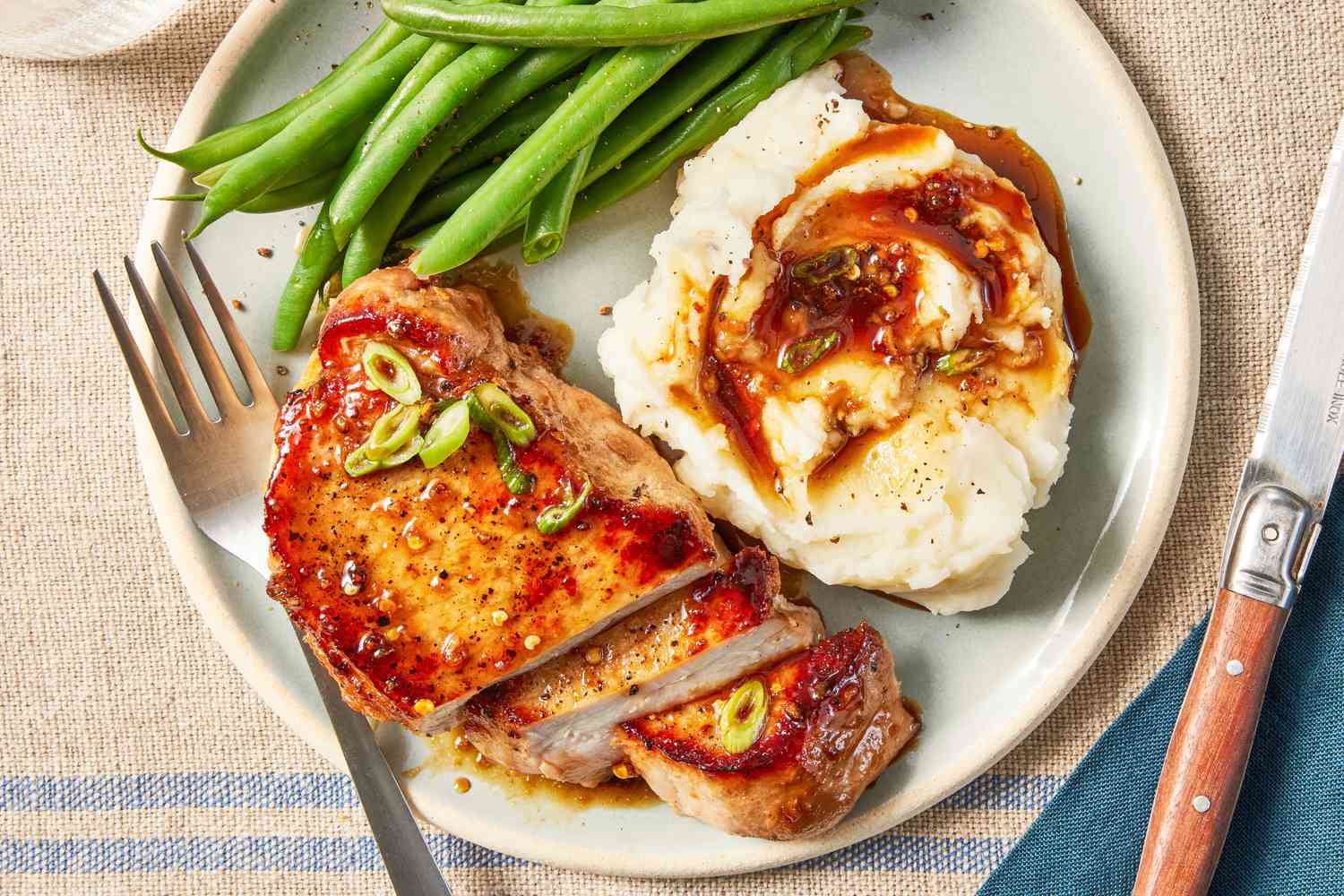 glazed pork chops served with mashed potatoes and green beans on a plate at a dinner table