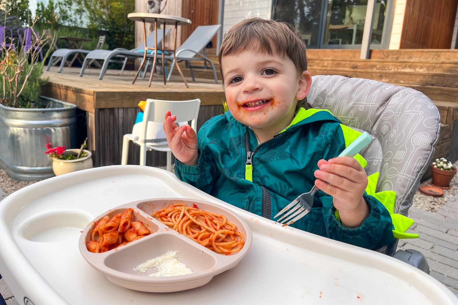 A two-year-old kid eating pasta, with red pasta sauce all over his face