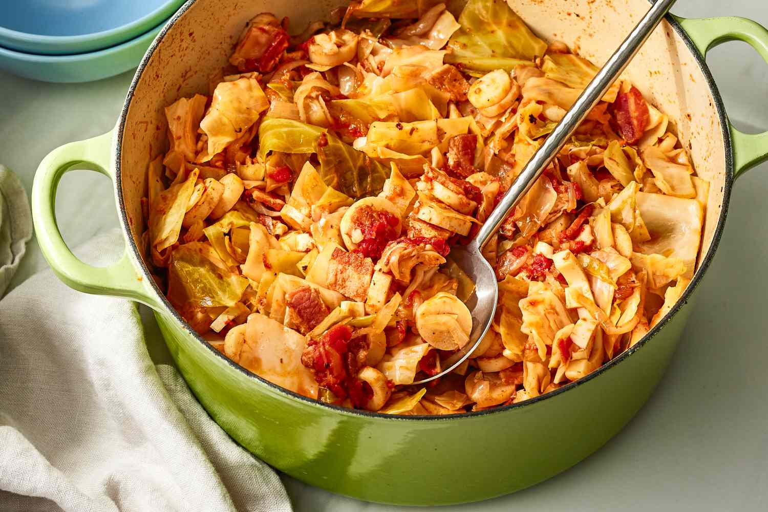 Angled view of a green dutch oven of swamp cabbage with a metal serving spoon