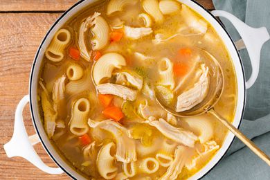 A pot of macaroni chicken sopas (Filipino chicken noodle soup), with a golden serving spoon scooping some soup out