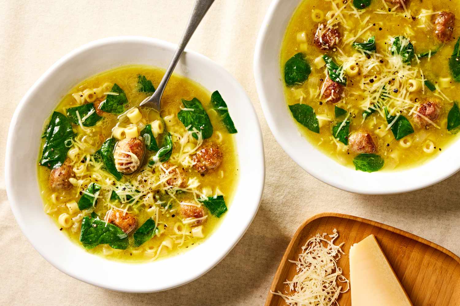Overhead view of a two white bowls of Italian wedding soup topped with Parmesan cheese
