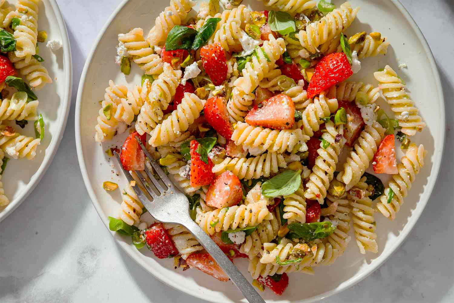 Plate of fusilli pasta salad with strawberries and greens fork placed on the side