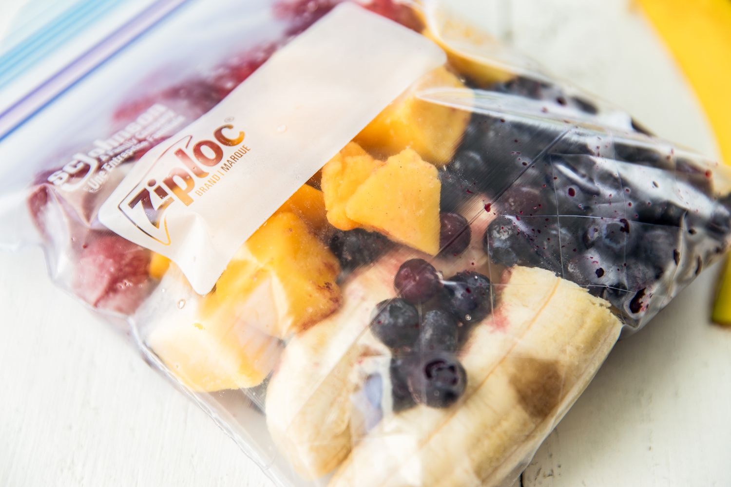A sealed plastic bag containing a mix of chopped banana, blueberries, and mango pieces