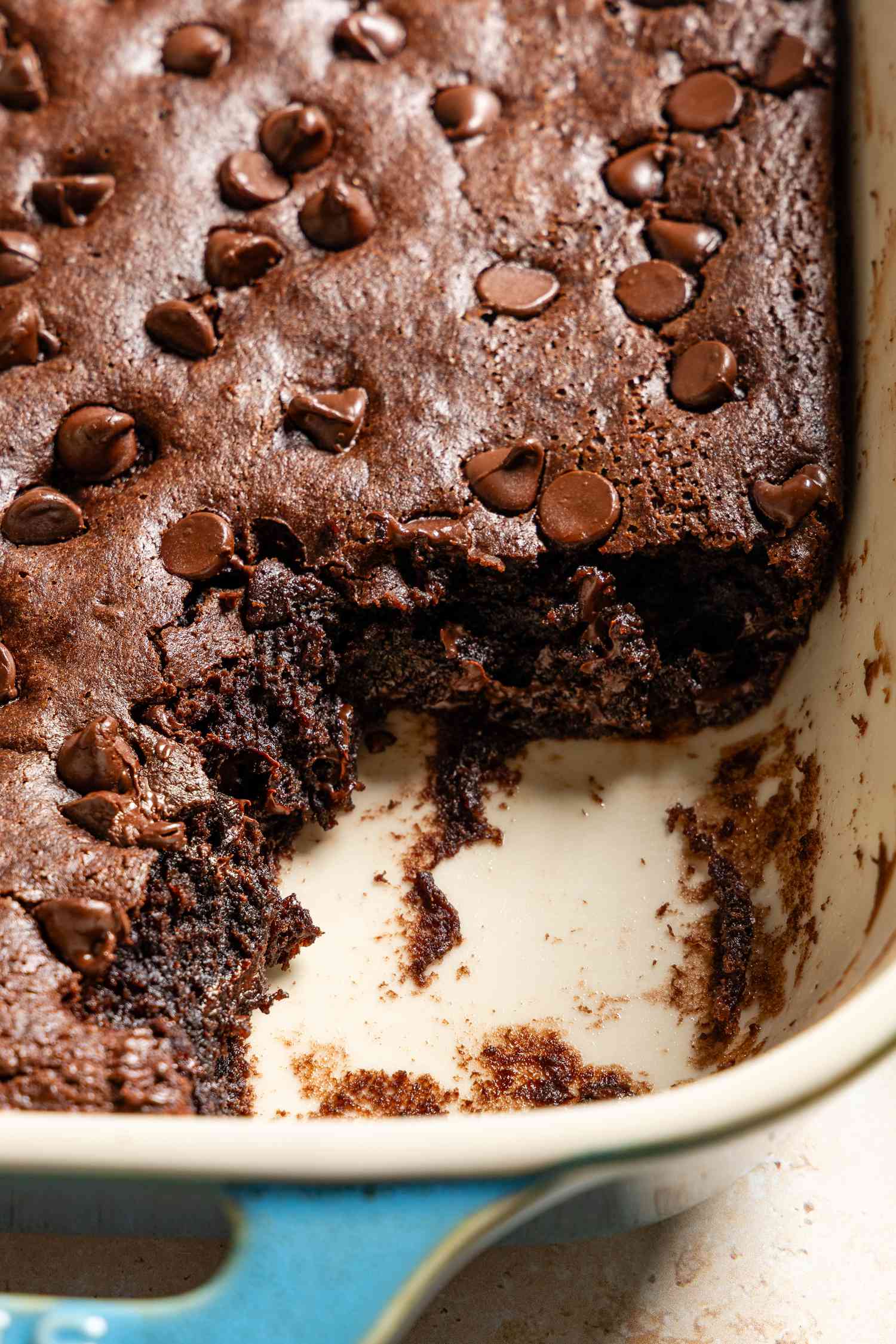 Closeup view of a corner of a baking dish of baked batter with a slice removed for Chocolate Dump Cake recipe on a tan countertop