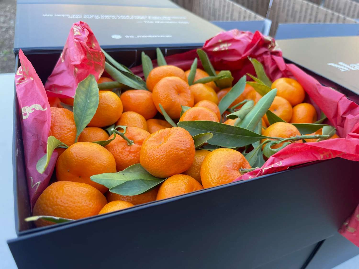 A box filled with fresh tangerines and green leaves wrapped in red tissue paper
