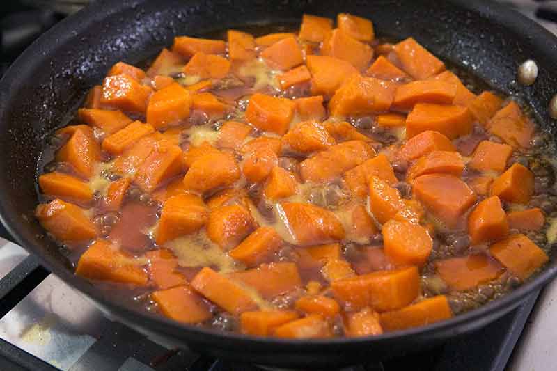 A skillet with candied yams cooking in a reduced syrup